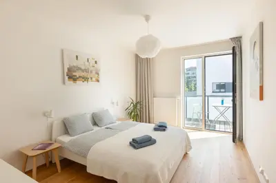 a white bedroom with a bed and a large window at Contemporary apartment with garage parking in Prague