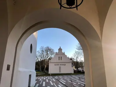 an archway leading to a white building with a clock tower at Olivův Pivovar in Dolní Břežany