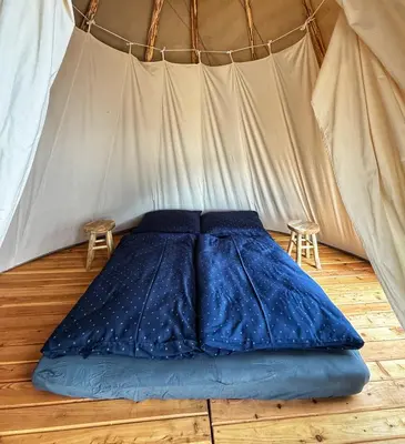a bed in a tent with two stools at Glamping TeePee in Brandýs nad Labem-Stará Boleslav
