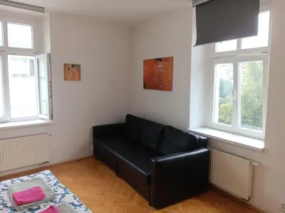 a living room with a black leather couch and two windows at Cosy appartment close to main train station and city center in Prague