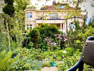 a building behind a garden with flowers and a bench at Villa Riviera in Prague