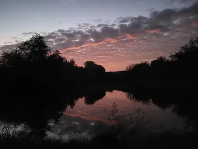 a sunset over a body of water with trees and clouds at Kempování s výhledem na hrady in Zdice