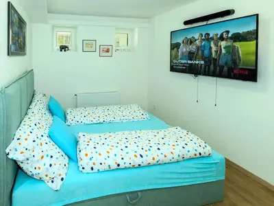 a bedroom with a blue bed with a tv on the wall at Apartment Hanspaulka - Stylish, Parking Included, 15 min Airport in Prague