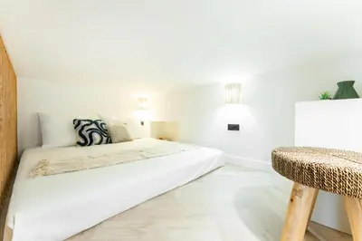 a white bedroom with a bed and a chair at Rentero Lublanska Residence - Stylish Lofts in Prague