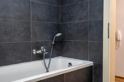 a bath tub with a shower head in a bathroom at The Green Loft Studio - 10 min to City Center in Prague