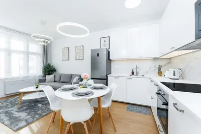 a white kitchen and living room with a table and chairs at Rentero Warm and Bright Apartment at Prague in Prague