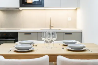 a wooden table with plates and a wine glass at Rentero NEW Anděl Skyline Apartment - Prague 5 in Prague