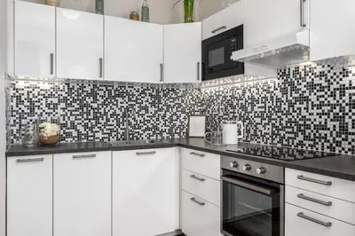 a kitchen with white cabinets and a black and white tile wall at Serenity Suite Prague in Prague
