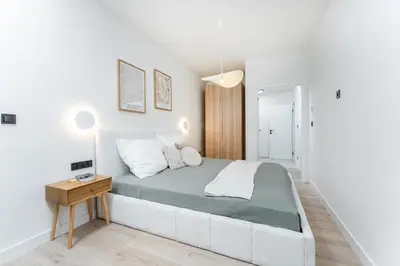 a white bedroom with a bed and a wooden table at Rentero Riverside Serenity Residence - Prague 7 in Prague