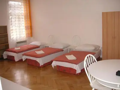 three beds in a room with a table and chairs at Hostel Bell in Prague