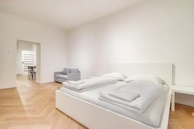 a white bedroom with a white bed and a chair at Modern City Apartment with Balcony by Rentez in Prague