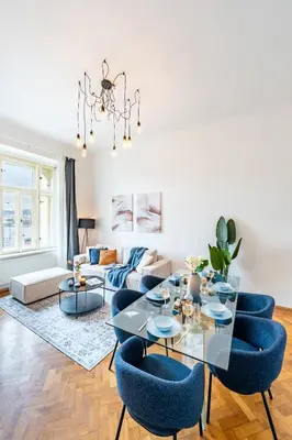 a living room with a glass table and blue chairs at Prague Days - Riverside Two-Bedroom Apartment with Workspace in New Town in Prague