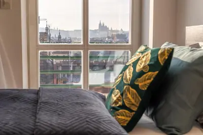 a couch with two pillows in front of a window at Skyline 127m Residence with Terrace - Prague Castle View in Prague