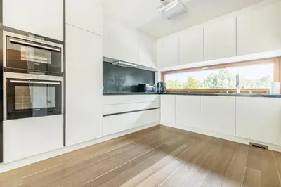 a kitchen with white cabinets and a wooden floor at Prague Airport Luxury Vila in Prague