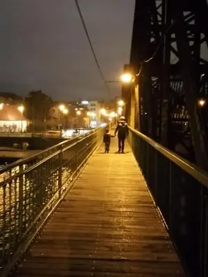 a person walking down a bridge at night at ANDĚL apartment VLTAVA' SPIRIT - Smíchov in Prague