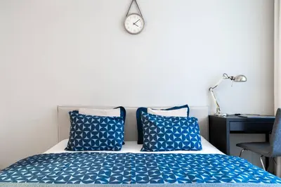 a bed with blue pillows and a clock on the wall at Apartment near PVA Expo Prague & Concerts in Prague