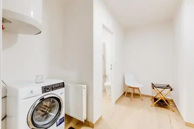 a washing machine in a white laundry room with a chair at Comfy Apartment with Bedroom Nook in Prague