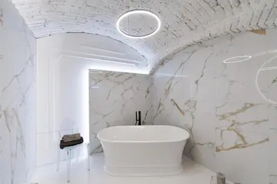 a bathroom with a white tub and a white marble wall at Vaulted Luxury Retreat in Prague