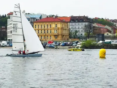 a small sail boat in the water with buildings at Central river view in Prague