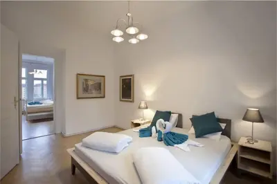 a white bedroom with a large white bed with blue pillows at Spectacular Riverview apartment in Prague