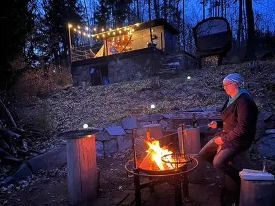 a man sitting around a fire in front of a cabin at Tinyhouse Veranda