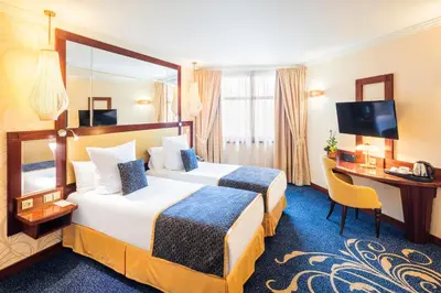 a hotel room with two beds and a desk at Occidental Praha Wilson in Prague