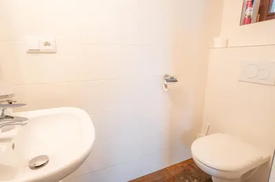 a white bathroom with a toilet and a sink at Rooms & Restaurace Na Jitrách in Semice