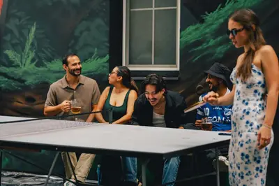 a group of people standing around a ping pong table at Drunken Monkey Hostel in Prague