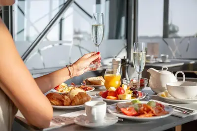 a woman holding a champagne glass at a table with food at Dancing House - Tančící dům hotel in Prague