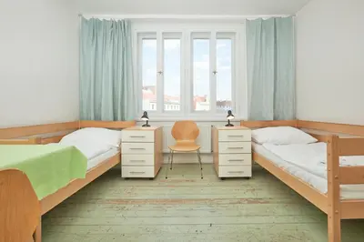 a bedroom with two beds and a chair and a window at Hostel Mikoláše Alše in Prague