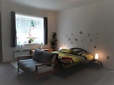 a bedroom with a bed and a chair and a window at Apartmány Karlštejn in Karlštejn