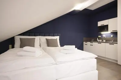 a bedroom with a large white bed and a kitchen at Alveo Suites in Prague