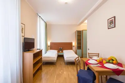 a living room with a table and a room with a bed and a television at Duskova Apartments in Prague