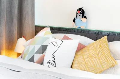 a bed with colorful pillows and a stuffed penguin on a shelf at MOSAIC HOUSE Design Hotel in Prague