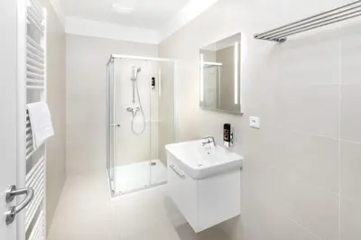 a white bathroom with a shower and a sink at DownTown Suites Belohorska in Prague