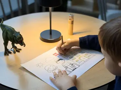 a young boy is sitting at a table drawing a dinosaur at Ibis Praha Mala Strana in Prague