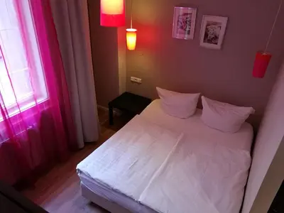 a small bedroom with a white bed with pink lighting at Hotel PurPur in Prague