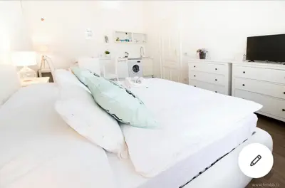 a white bedroom with a bed with pillows and a tv at Romantic Apartment Petra - free parking Friday-Sunday in Prague