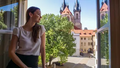 a woman looking out of a window at a church at Josephine Old Town Square Hotel - Czech Leading Hotels in Prague