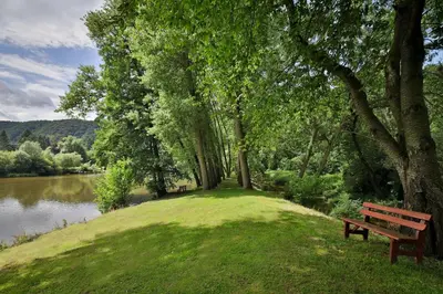 a park bench sitting on the grass next to a lake at Penzion Karlštejn in Karlštejn