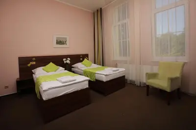 a room with two beds and a chair and a window at Hotel Zámeček in Poděbrady