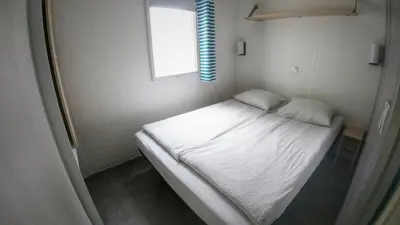 a small bedroom with a white bed with a window at Camping Sokol Praha in Prague