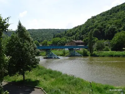 a blue bridge over a river with a mountain at Hotel U Berounky in Srbsko