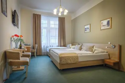 a bedroom with two beds and a chair and a window at Hotel Taurus in Prague