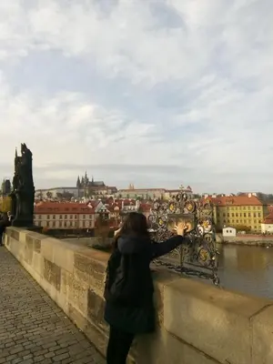 a woman standing on a bridge taking a picture of a city at apartricanova in Prague