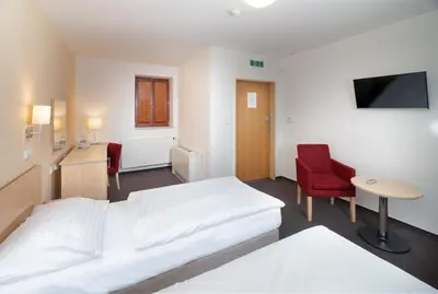 a hotel room with a white bed and a red chair at Hotel Chvalská Tvrz in Prague