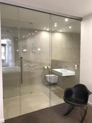 a glass shower in a bathroom with a sink and a chair at Rozmaryn Hotel B&B in Rakovník