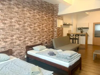 a room with two beds and a chair and a brick wall at Žižkov Cosy Studio Apartments in Prague