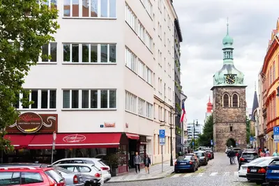 a busy city street with cars parked on the sidewalk and a clock tower at 4 Elements Apartments in Prague
