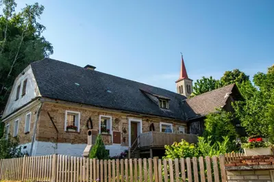 an old house with a church steeple behind a fence at Kamenný dům Bezdědice-Máchův kraj in Bezdědice